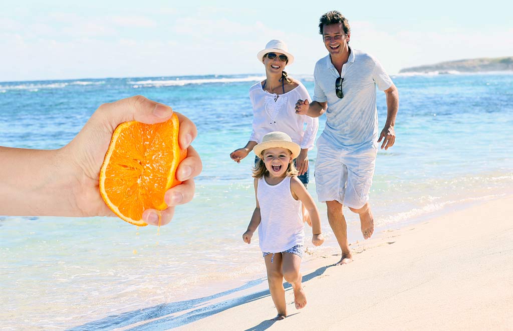 Someone squeezing an orange in front of a family on the beach.